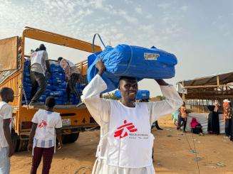 A man carries plastic sheeting to distribute in a displacement camp in Chad. 