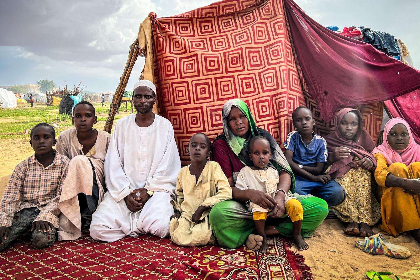 A family of Sudanese refugees sit in front of a makeshift tent in a refugee camp in Chad