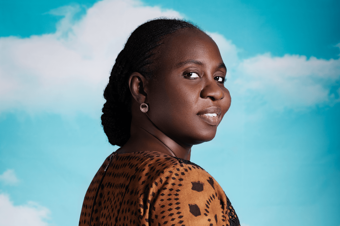 A woman smiling and looking back against a sky blue background.